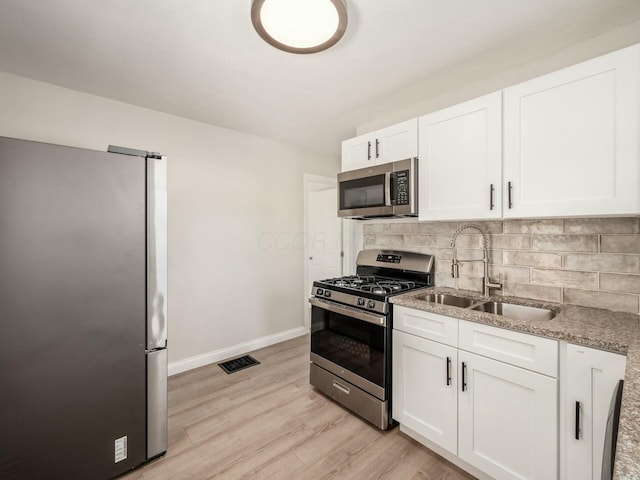 kitchen with white cabinets, stainless steel appliances, light stone countertops, decorative backsplash, and sink