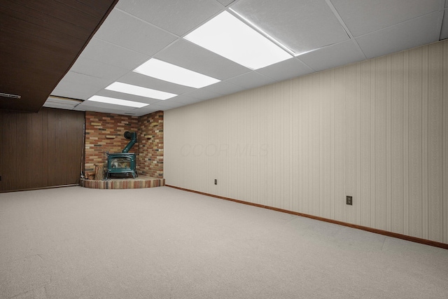 unfurnished living room featuring a paneled ceiling, carpet floors, and a wood stove