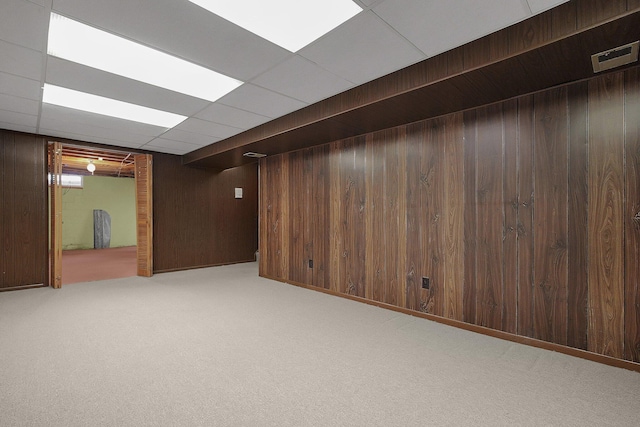 basement featuring wood walls, a drop ceiling, and light colored carpet