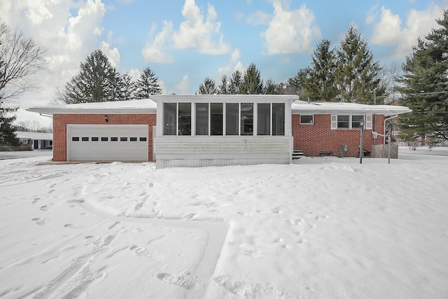 snow covered rear of property featuring a sunroom and a garage