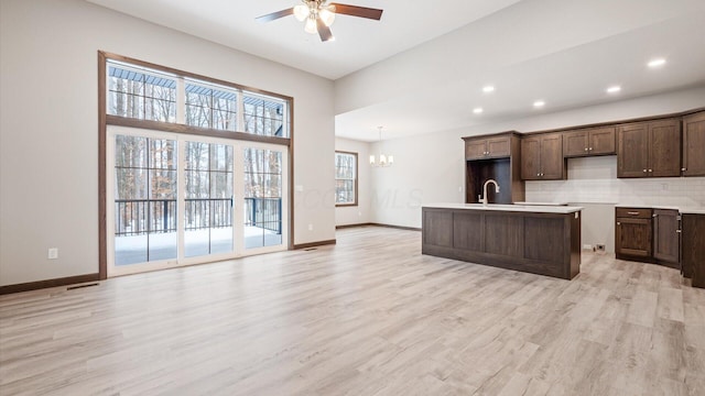 kitchen with tasteful backsplash, light wood-type flooring, an island with sink, sink, and ceiling fan with notable chandelier