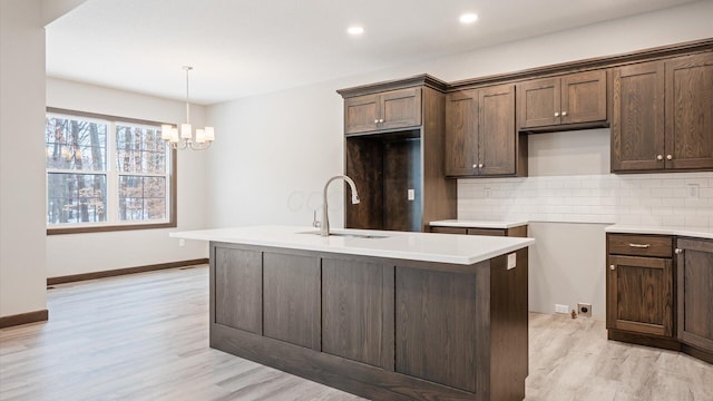 kitchen with hanging light fixtures, a center island with sink, light hardwood / wood-style floors, decorative backsplash, and sink