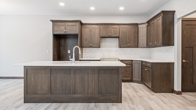 kitchen with light wood-type flooring, a kitchen island with sink, decorative backsplash, and sink