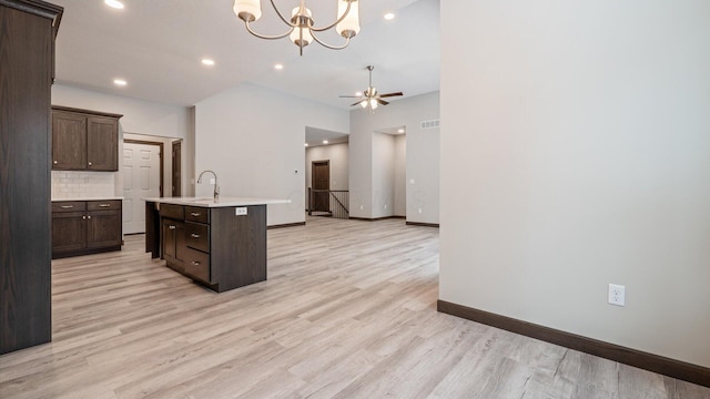 kitchen featuring light hardwood / wood-style floors, a kitchen island with sink, ceiling fan with notable chandelier, and dark brown cabinetry