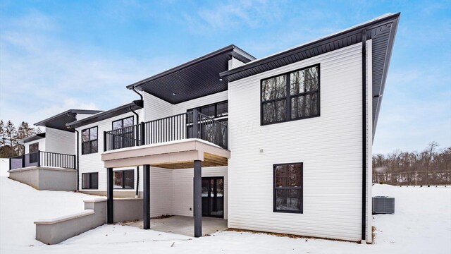 snow covered rear of property featuring a balcony and central air condition unit