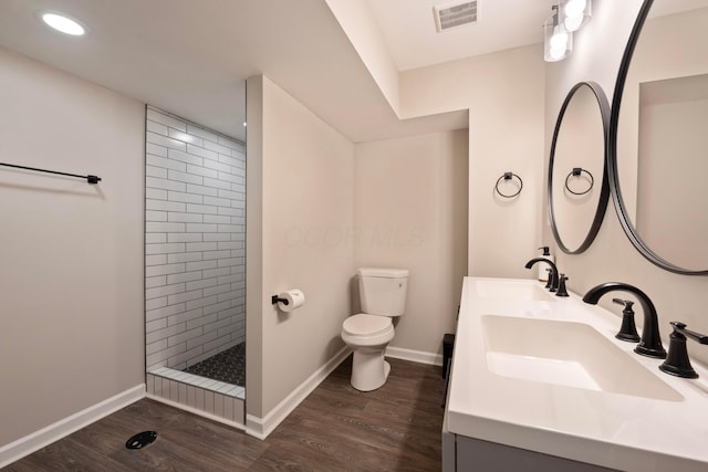 bathroom with toilet, wood-type flooring, tiled shower, and vanity