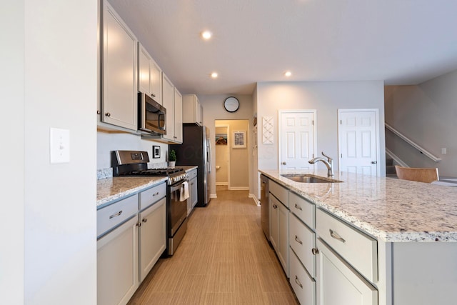 kitchen featuring light stone countertops, sink, stainless steel appliances, and a center island with sink