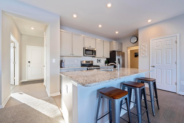 kitchen with a kitchen bar, an island with sink, stainless steel appliances, light stone countertops, and sink