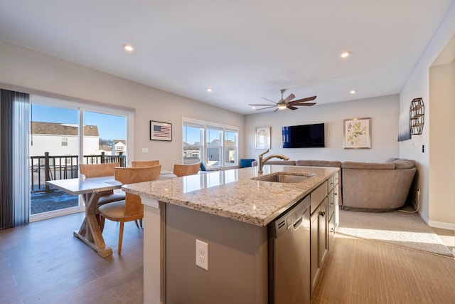 kitchen with ceiling fan, dishwasher, a center island with sink, sink, and light stone counters