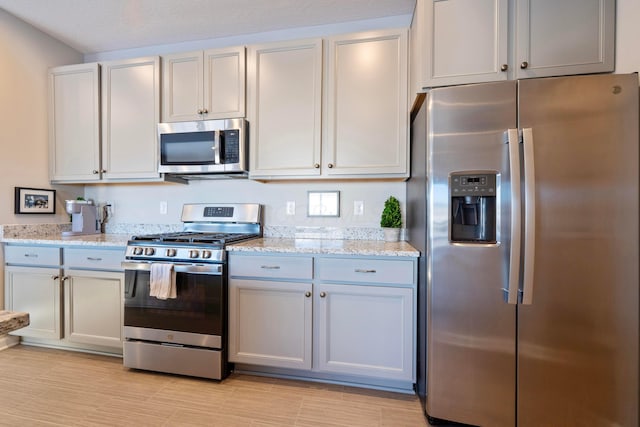 kitchen with light stone countertops, white cabinetry, and stainless steel appliances