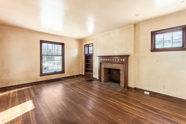 unfurnished living room with dark hardwood / wood-style flooring, a brick fireplace, and plenty of natural light