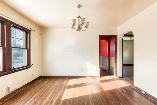 spare room featuring wood-type flooring and an inviting chandelier