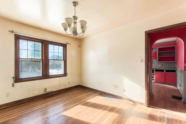 spare room featuring wood-type flooring and a chandelier