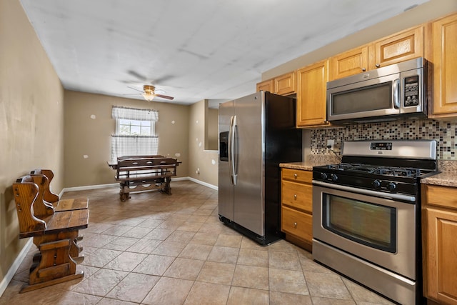 kitchen with ceiling fan, appliances with stainless steel finishes, backsplash, and light stone countertops