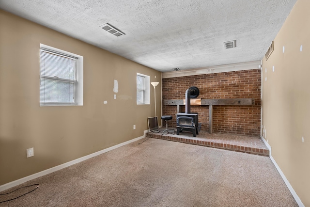 unfurnished living room featuring carpet floors, a wood stove, and a textured ceiling