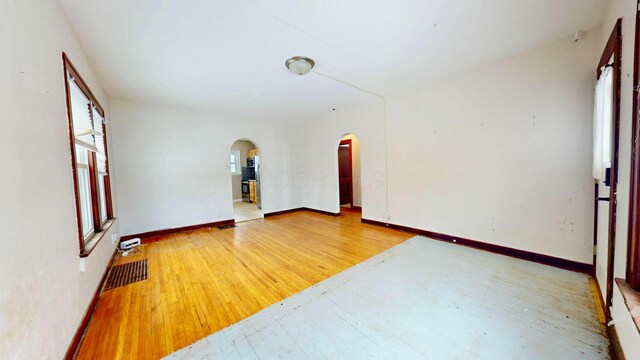 empty room featuring light wood-type flooring, arched walkways, visible vents, and baseboards