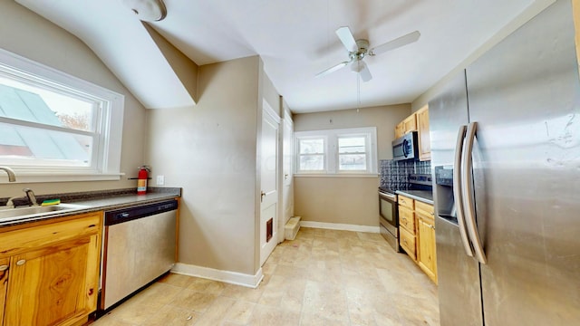 kitchen with dark countertops, baseboards, appliances with stainless steel finishes, and a sink