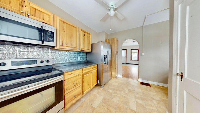 kitchen with arched walkways, ceiling fan, appliances with stainless steel finishes, backsplash, and dark countertops