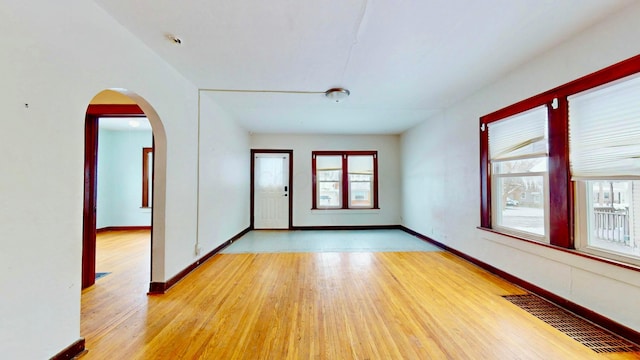 unfurnished room featuring arched walkways, a wealth of natural light, light wood-type flooring, and visible vents