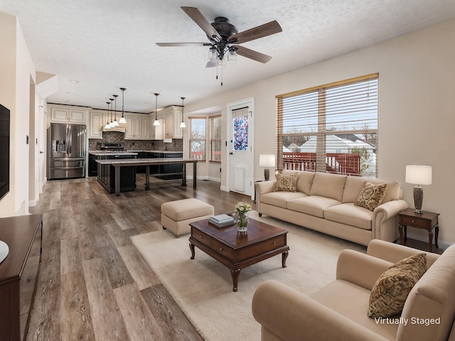 living room with a textured ceiling, ceiling fan, and wood-type flooring