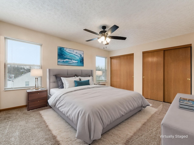 carpeted bedroom featuring ceiling fan, multiple closets, and a textured ceiling