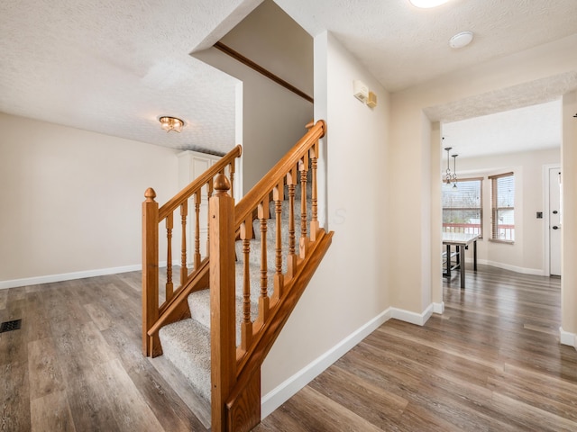 stairs with wood-type flooring, a textured ceiling, and an inviting chandelier