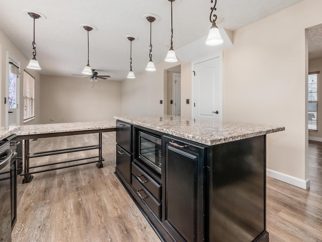 kitchen featuring a center island, decorative light fixtures, light wood-type flooring, ceiling fan, and built in microwave