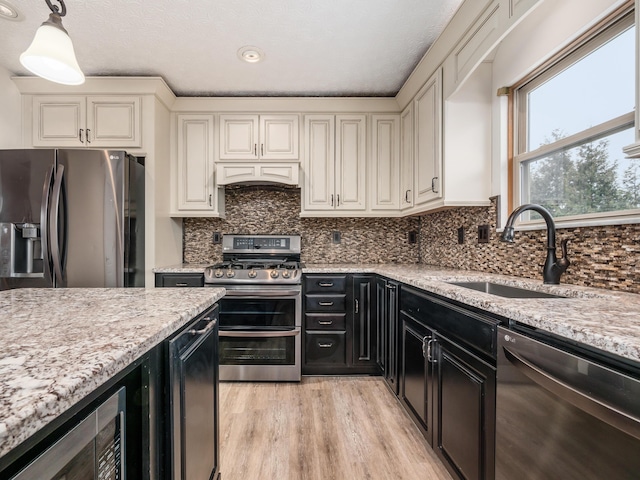 kitchen featuring hanging light fixtures, appliances with stainless steel finishes, sink, and light stone counters