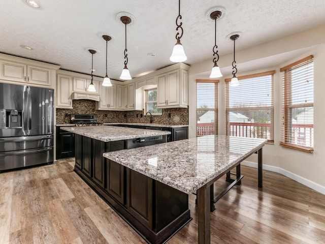 kitchen featuring decorative light fixtures, appliances with stainless steel finishes, cream cabinetry, and a kitchen island