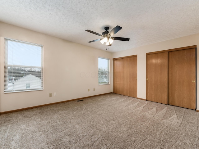 unfurnished bedroom featuring ceiling fan, light carpet, multiple closets, and a textured ceiling