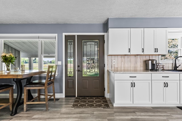 kitchen featuring white cabinets, a textured ceiling, light hardwood / wood-style flooring, and tasteful backsplash