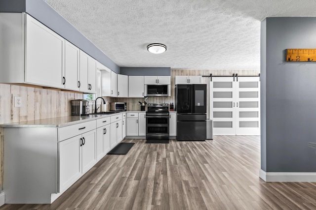 kitchen with a barn door, appliances with stainless steel finishes, light wood-type flooring, sink, and white cabinetry