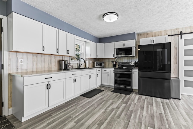 kitchen featuring a barn door, stainless steel appliances, sink, light hardwood / wood-style flooring, and white cabinetry