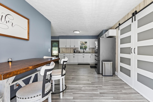 kitchen featuring sink, white cabinets, decorative backsplash, a barn door, and stainless steel fridge