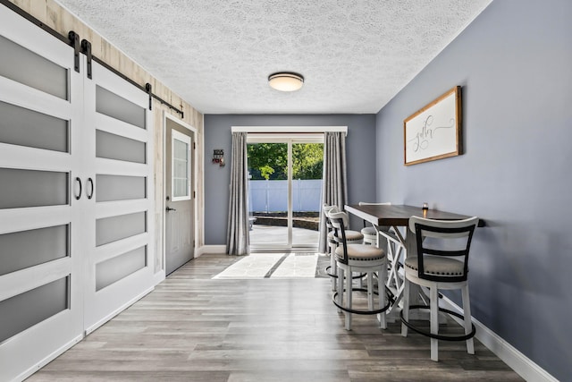 dining space with a textured ceiling, a barn door, and wood-type flooring