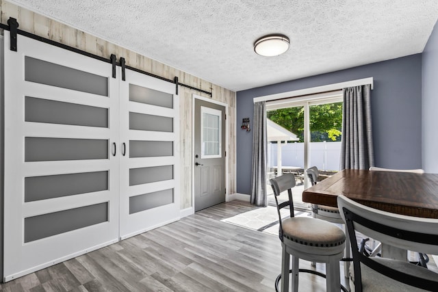 dining area featuring light wood-type flooring, a textured ceiling, a barn door, and wooden walls