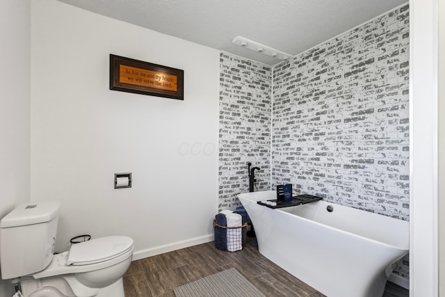 bathroom with a textured ceiling, a tub to relax in, toilet, and hardwood / wood-style flooring