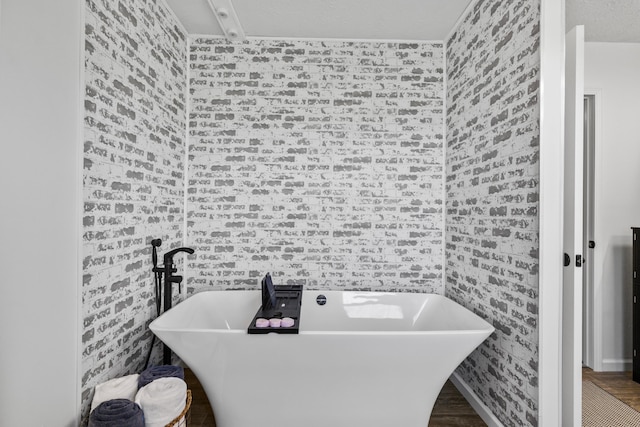 bathroom featuring a tub to relax in, brick wall, and wood-type flooring