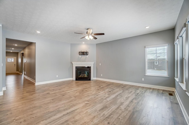 unfurnished living room with a textured ceiling, light wood-type flooring, and ceiling fan