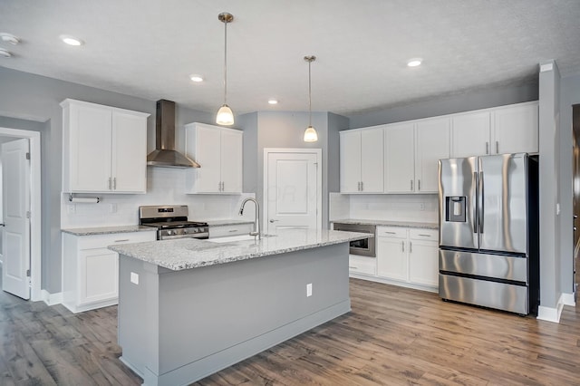 kitchen featuring white cabinets, wall chimney exhaust hood, hanging light fixtures, a kitchen island with sink, and appliances with stainless steel finishes