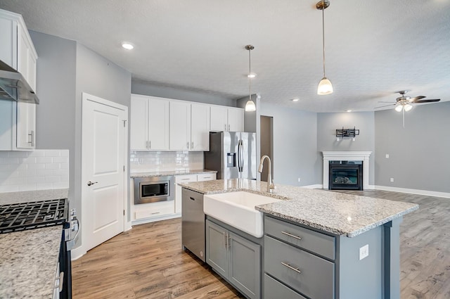 kitchen with a center island with sink, appliances with stainless steel finishes, hanging light fixtures, decorative backsplash, and white cabinetry