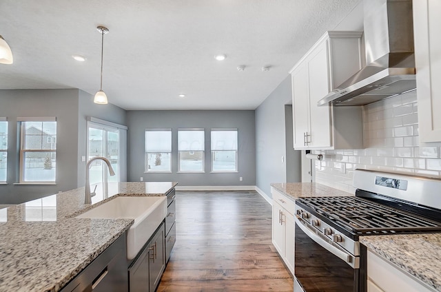 kitchen with light stone countertops, decorative light fixtures, wall chimney range hood, white cabinetry, and appliances with stainless steel finishes