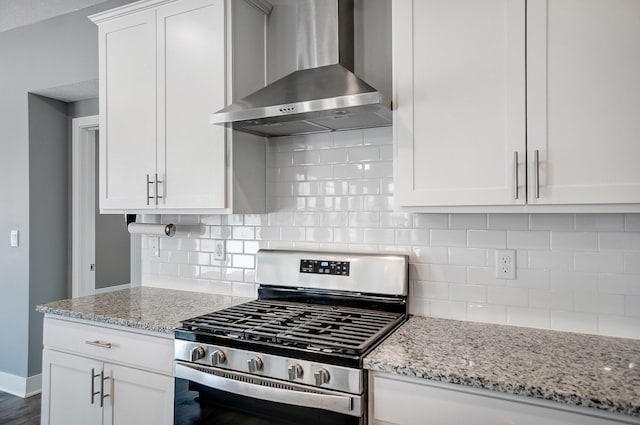 kitchen featuring stainless steel range with gas stovetop, light stone counters, white cabinets, wall chimney range hood, and backsplash