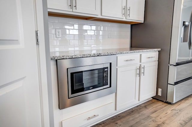 kitchen with light wood-type flooring, light stone countertops, decorative backsplash, stainless steel microwave, and white cabinetry