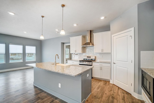 kitchen featuring a center island with sink, wall chimney exhaust hood, sink, stainless steel range oven, and white cabinetry