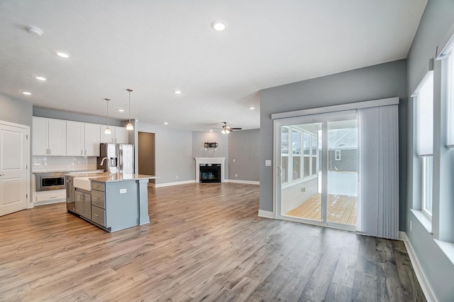 kitchen featuring stainless steel appliances, white cabinetry, light stone counters, an island with sink, and hanging light fixtures