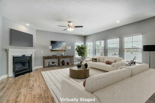 living room with a textured ceiling, ceiling fan, and wood-type flooring