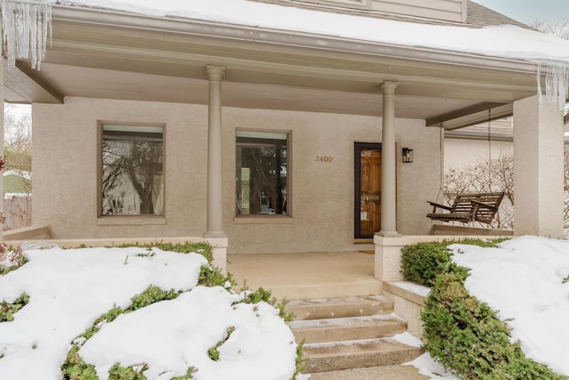 snow covered property entrance with a porch