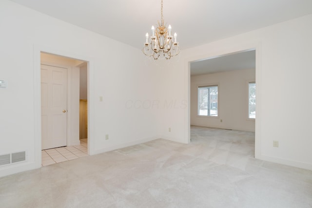 spare room featuring light carpet and an inviting chandelier