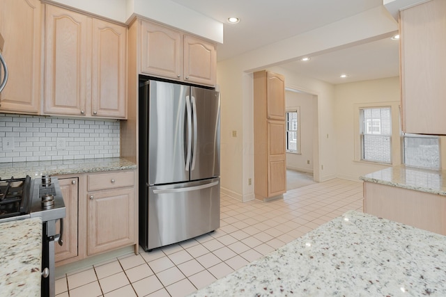 kitchen with light brown cabinetry, light stone countertops, stainless steel fridge, and tasteful backsplash